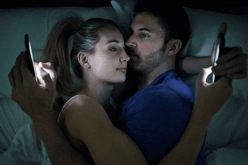 couples in bed together holding their phones